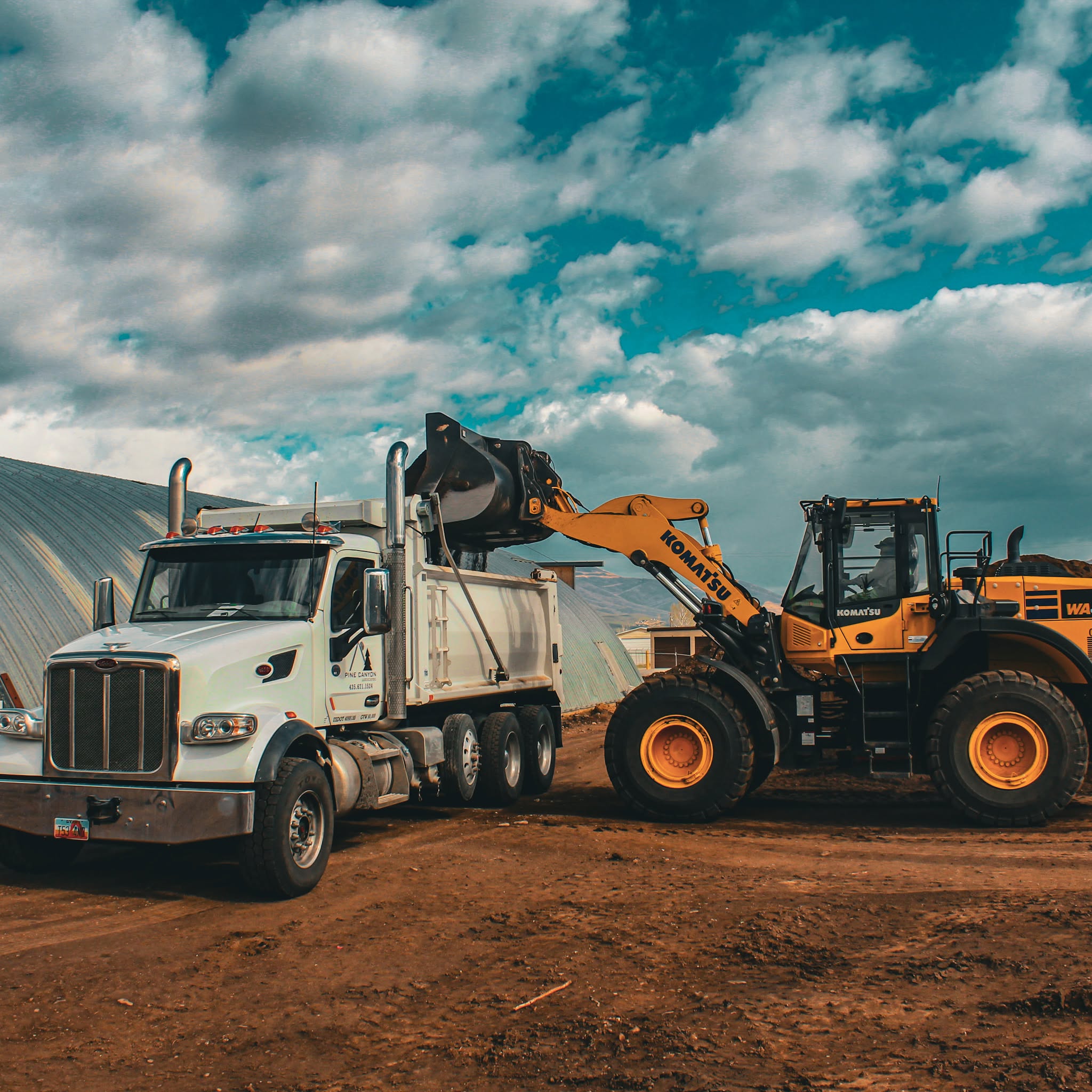 Pine Canyon loader filling a branded dump truck at the Heber City landscape material yard
